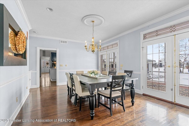 dining area with crown molding, dark wood-type flooring, a notable chandelier, a textured ceiling, and french doors