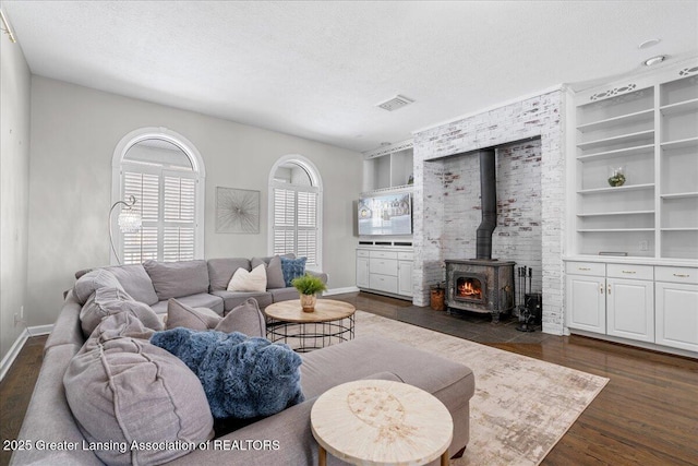 living room featuring dark wood-type flooring, a wood stove, and a textured ceiling