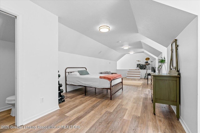 bedroom featuring lofted ceiling, ensuite bathroom, a textured ceiling, and light wood-type flooring