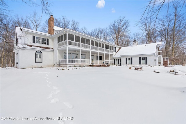 snow covered rear of property featuring a sunroom and a porch