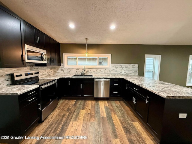 kitchen with decorative light fixtures, sink, kitchen peninsula, stainless steel appliances, and a textured ceiling