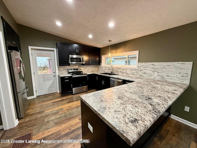 kitchen featuring lofted ceiling, decorative light fixtures, kitchen peninsula, stainless steel appliances, and light stone countertops