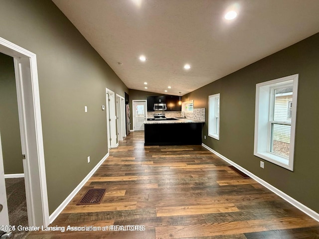 kitchen featuring lofted ceiling, dark wood-type flooring, stainless steel appliances, decorative backsplash, and kitchen peninsula