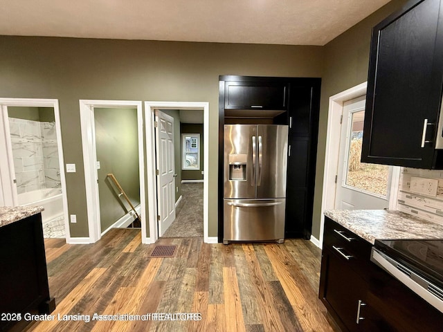 kitchen with stainless steel refrigerator with ice dispenser, light stone countertops, dark wood-type flooring, and range with electric cooktop