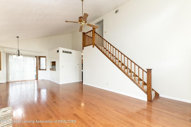 unfurnished living room featuring hardwood / wood-style flooring, ceiling fan with notable chandelier, and high vaulted ceiling