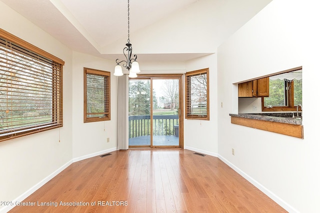 unfurnished dining area featuring lofted ceiling, a notable chandelier, and light hardwood / wood-style flooring