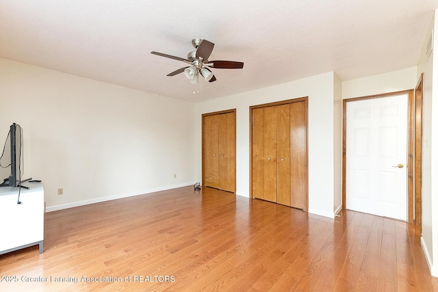 unfurnished bedroom with two closets, a textured ceiling, ceiling fan, and hardwood / wood-style flooring