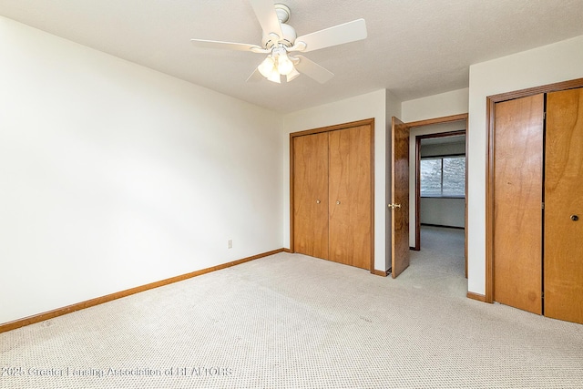 unfurnished bedroom featuring ceiling fan, light carpet, and two closets