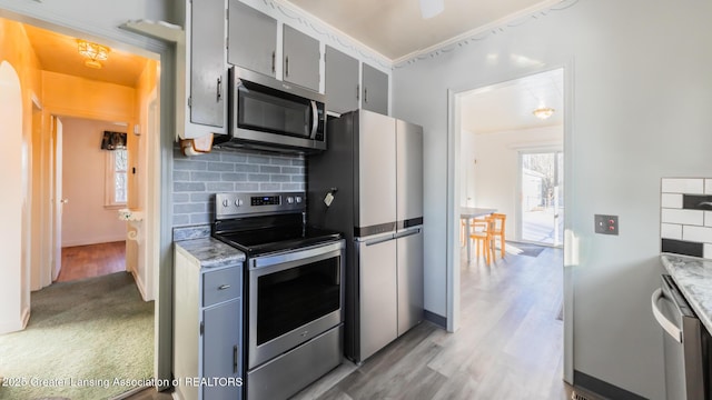 kitchen with gray cabinets, stainless steel appliances, tasteful backsplash, ornamental molding, and light colored carpet