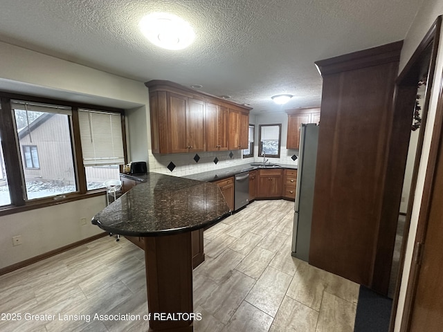 kitchen featuring a kitchen bar, sink, a textured ceiling, kitchen peninsula, and stainless steel appliances