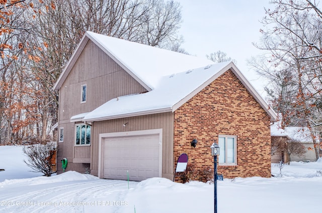 view of snow covered exterior with brick siding and an attached garage