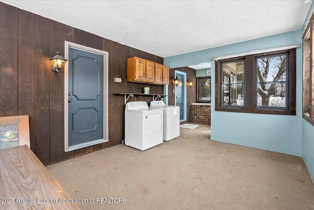 clothes washing area with wood walls, separate washer and dryer, cabinets, light carpet, and a textured ceiling