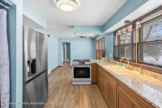 kitchen featuring sink, hanging light fixtures, light wood-type flooring, appliances with stainless steel finishes, and light stone countertops