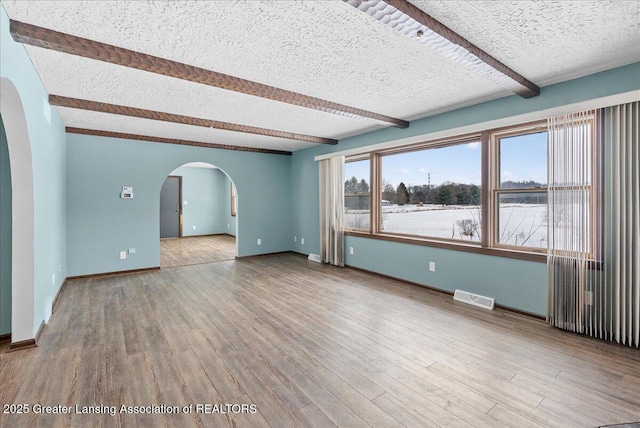 spare room with hardwood / wood-style floors, a textured ceiling, and beamed ceiling