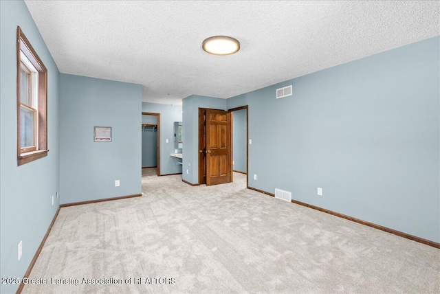 unfurnished bedroom featuring light carpet, a walk in closet, a closet, and a textured ceiling