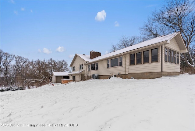 snow covered back of property featuring a sunroom