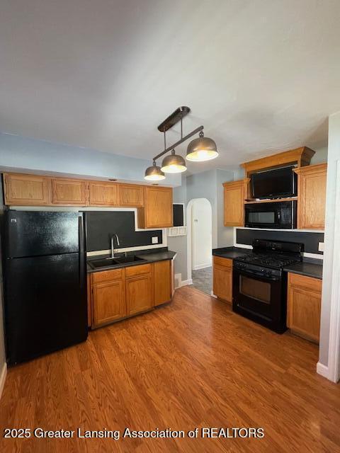 kitchen with sink, hanging light fixtures, black appliances, and hardwood / wood-style floors