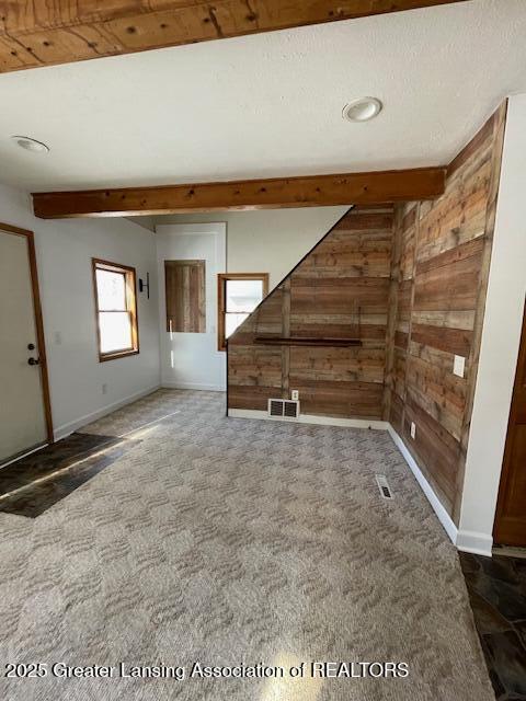 carpeted spare room featuring beamed ceiling and wooden walls