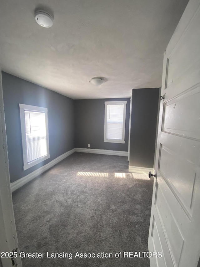 unfurnished room featuring plenty of natural light and dark colored carpet