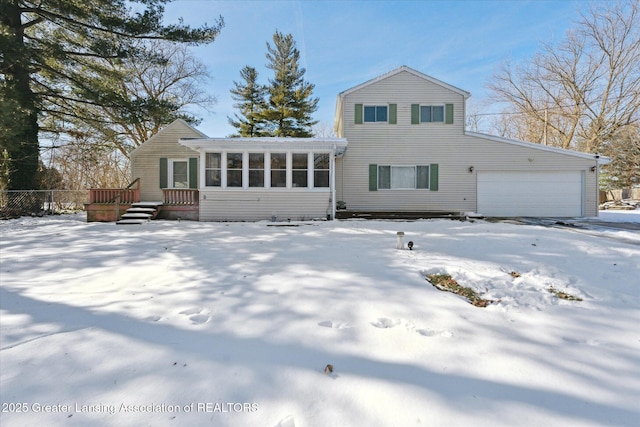 snow covered house with a wooden deck, a garage, and a sunroom