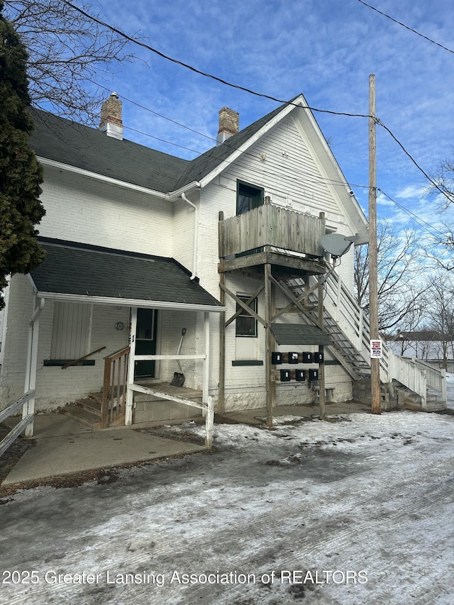 view of front of home featuring a shingled roof, brick siding, and a balcony