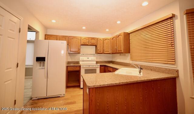 kitchen with sink, white appliances, light stone counters, light hardwood / wood-style floors, and kitchen peninsula