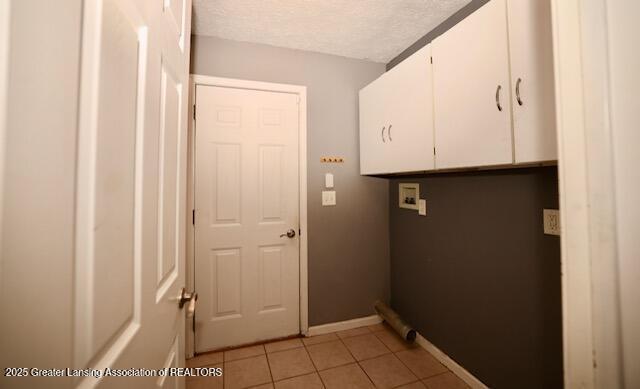 clothes washing area featuring light tile patterned flooring, cabinets, washer hookup, and a textured ceiling