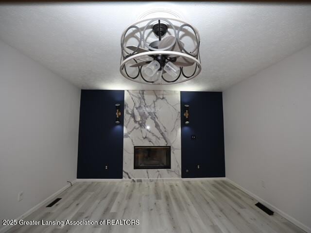 unfurnished living room featuring a premium fireplace, a textured ceiling, and light wood-type flooring