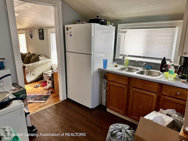 kitchen with vaulted ceiling, sink, dark hardwood / wood-style flooring, white refrigerator, and a textured ceiling