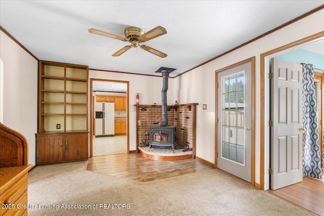 carpeted living room with ornamental molding, ceiling fan, and a wood stove