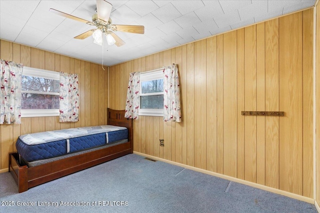 unfurnished bedroom featuring multiple windows, carpet floors, ceiling fan, and wood walls