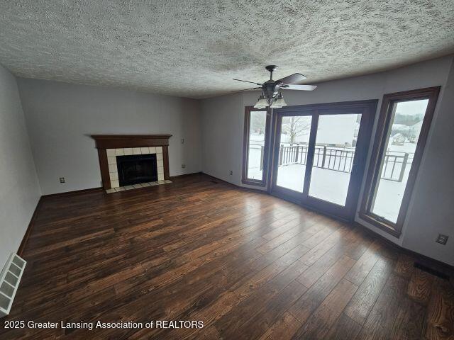 unfurnished living room featuring ceiling fan, dark hardwood / wood-style floors, a tile fireplace, and a textured ceiling