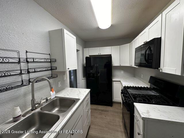 kitchen featuring sink, white cabinets, dark hardwood / wood-style flooring, black appliances, and a textured ceiling