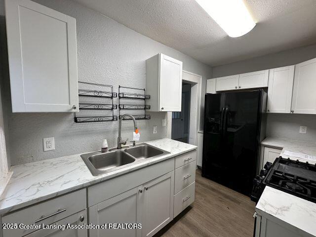 kitchen with sink, black fridge with ice dispenser, a textured ceiling, and white cabinets