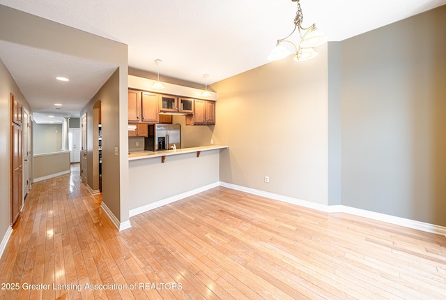 kitchen with a kitchen bar, stainless steel fridge with ice dispenser, hanging light fixtures, light hardwood / wood-style flooring, and kitchen peninsula