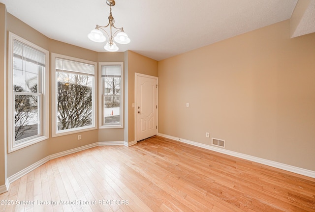 empty room with a chandelier and light wood-type flooring