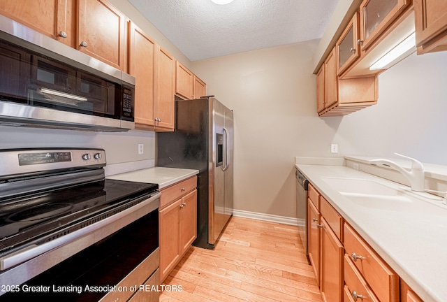 kitchen with appliances with stainless steel finishes, sink, a textured ceiling, and light wood-type flooring