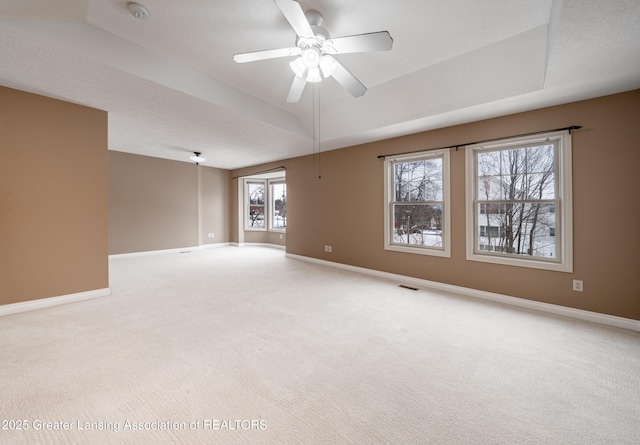 empty room with ceiling fan, a raised ceiling, and light carpet