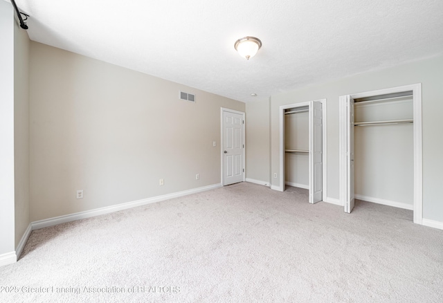 unfurnished bedroom with two closets, light colored carpet, and a textured ceiling