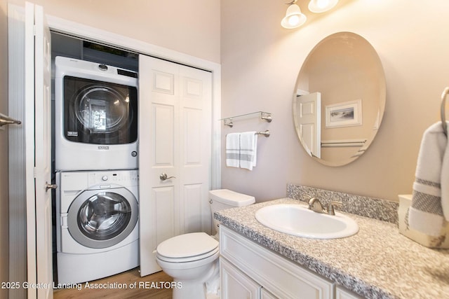 bathroom featuring hardwood / wood-style flooring, vanity, stacked washer / drying machine, and toilet