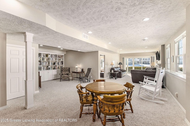 dining space with decorative columns, carpet floors, and a textured ceiling