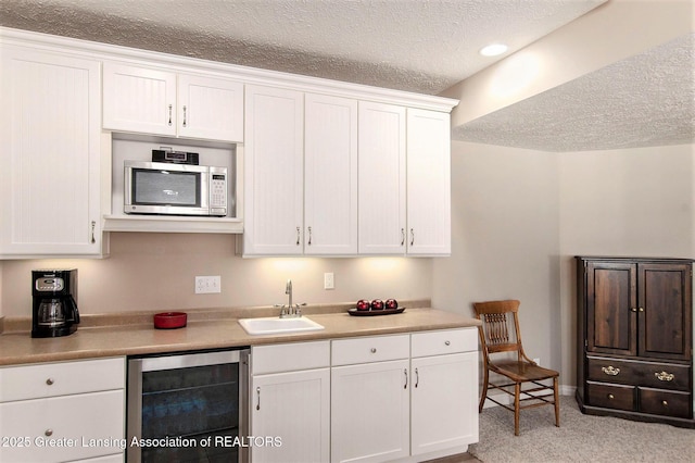 kitchen with white cabinets, sink, beverage cooler, and a textured ceiling