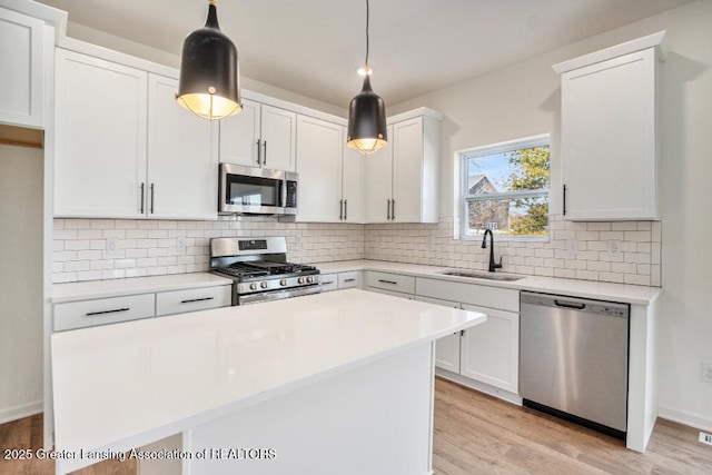 kitchen featuring appliances with stainless steel finishes, a center island, light wood-style floors, and a sink