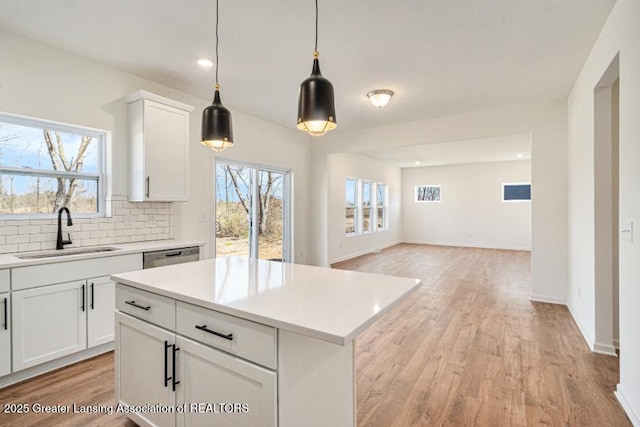 kitchen featuring light wood-style flooring, a sink, light countertops, dishwasher, and backsplash