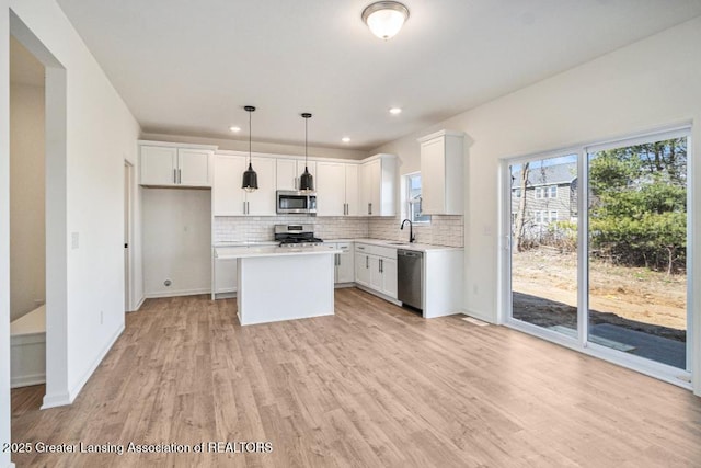 kitchen featuring a sink, backsplash, appliances with stainless steel finishes, light wood finished floors, and light countertops