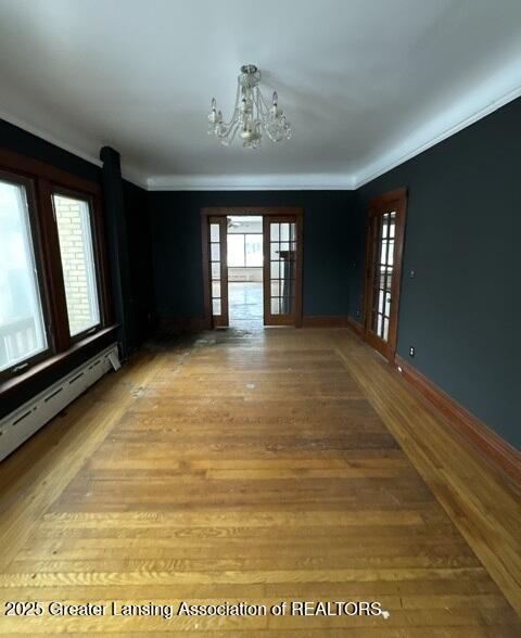 spare room with ornamental molding, wood-type flooring, a notable chandelier, and baseboard heating