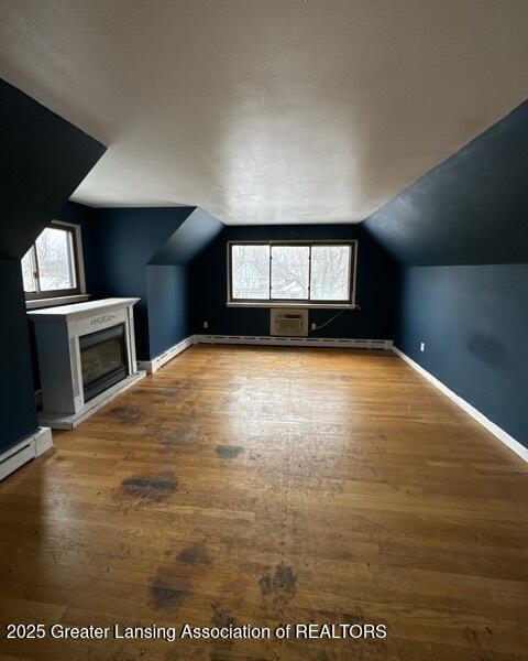 additional living space featuring lofted ceiling, hardwood / wood-style floors, and a baseboard heating unit