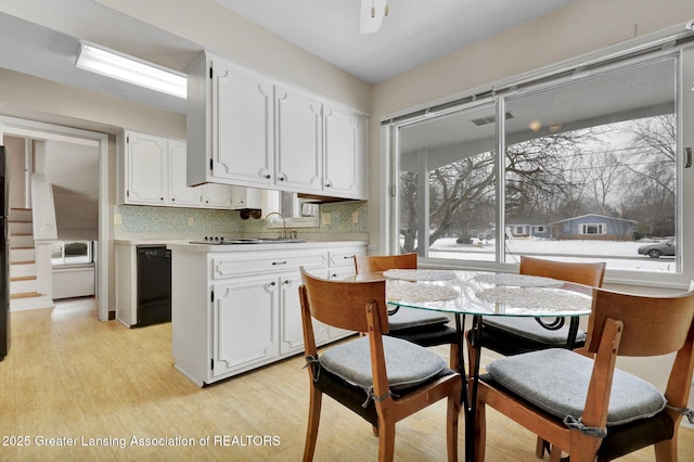 kitchen featuring sink, light hardwood / wood-style flooring, black dishwasher, white cabinets, and backsplash