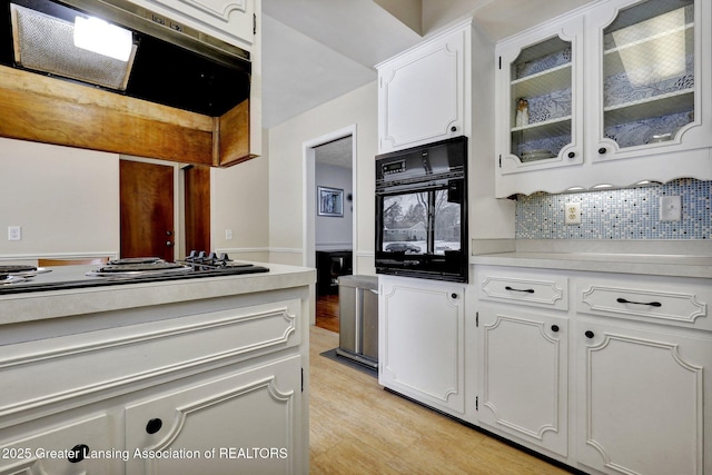 kitchen featuring ventilation hood, white gas stovetop, oven, decorative backsplash, and white cabinets