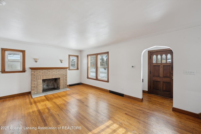 unfurnished living room featuring a brick fireplace, hardwood / wood-style flooring, ornamental molding, and a healthy amount of sunlight